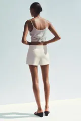Falda pantalón corta color crema, de tiro medio con abertura en el delantero y cierre lateral con cremallera.