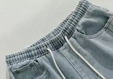 Pantalón de jean negro lavado, corte ancho y holgado, con cintura elástica y cordón ajustable. Presenta costuras verticales marcadas en los laterales exteriores de las piernas.