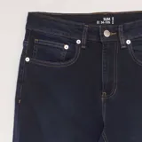 Pantalón de jean azul oscuro, corte slim, con bolsillos delanteros y traseros y costuras en color ocre.