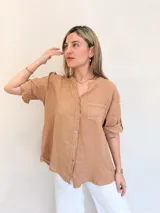 Camisa color marrón claro de lino, con cuello mao, manga corta con botón para enrollar, cierre frontal con botones y bolsillo de parche en el pecho.