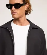 Campera negra de algodón con cuello inglés, cierre con cremallera, manga larga con ajuste fruncido elástico en el bajo trasero y bolsillos laterales.