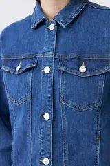 Campera clásica de jean color azul medio, con cuello clásico, cierre frontal con botones, bolsillos con solapa en el pecho y mangas largas con puños abotonados.