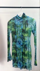 Minivestido de microtul celeste con estampado floral en tonos verdes y violetas, de mangas largas y cuello alto.