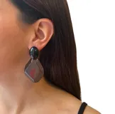 Aros colgantes con ajuste de perforación, hechos en resina italiana con acabado brillante y translúcido combinado. El aro superior es ovalado negro y el inferior es un romboide translúcido gris. Largo: 6 cm.