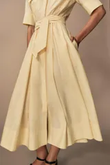 Vestido midi camisero color ladrillo, confeccionado en popelina de algodón. Presenta cuello solapa, manga corta con puños abotonados, bolsillos laterales ocultos y bolsillos de parche con solapa en el pecho. Incluye cinturón lazada en el mismo tejido y cierre frontal con botones ocultos.