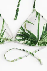 Top de bikini triangular blanco con estampado de hojas de palmera verdes y tirantes finos para atar al cuello y a la espalda.