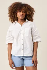 Camisa color beige claro, de corte clásico, con cuello, botones frontales, bolsillo en el pecho y mangas tres cuartos con presilla para sujetar.