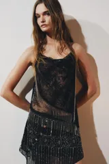 Falda corta negra de tiro medio, con bajo asimétrico. Presenta bordados y aplicaciones de abalorios en tonos plateados y dorados, con un diseño que incluye franjas verticales y motivos florales.