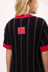 Vestido de tejido de punto, color negro con rayas verticales grises. Tiene cuello redondo y puños y ruedo en color rojo con costuras decorativas en hilo azul. Presenta un pequeño bordado de una letra 'B' estilizada en el pecho.