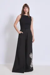 Pantalón negro de corte palazzo con apliques bordados en color crema en la parte inferior de una pierna.