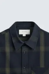 Camisa de hombre regular fit confeccionada en tejido de algodón a cuadros en tonos azul oscuro y verde oliva. Tiene cuello solapa, manga larga con puños abotonados, bolsillo de plastrón en el pecho y cierre frontal con botones.