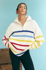 Sweater de punto grueso color crudo, con cuello alto con cierre de cremallera y rayas horizontales en azul, amarillo y rojo.