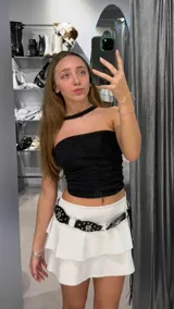 Minifalda blanca de tiro bajo con volados y cinturón negro con apliques metálicos.