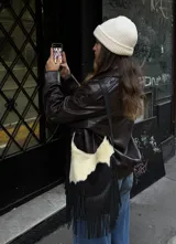 Cartera bandolera de cuero con pelo de vaca en blanco y negro y flecos largos de cuero negro. Tiene correa larga regulable para usar cruzada o al hombro, cierre y bolsillo interior.