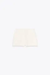 Falda pantalón corta color crema, de tiro medio con abertura en el delantero y cierre lateral con cremallera.