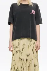 Camiseta de algodón color negro con efecto gastado (acid wash) y cuello redondo. Presenta un pequeño estampado en relieve color rosado en el pecho.