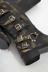 Botas de cuero gastado color marrón con hebillas y apliques de metal de caña alta.