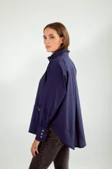 Camisa azul con cuello mao con volados, manga larga con puños con volados, cierre frontal con botones y bolsillo de parche con broche con forma de insecto.