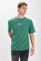 Remera verde con estampa frontal de la marca Roots en color blanco. Corte oversize y mangas cortas.
