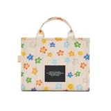 Bolso tote mediano de lona color crema con estampado de margaritas de colores. Tiene cierre superior con cremallera, asas superiores de lona resistente y correa de cincha ajustable y extraíble.