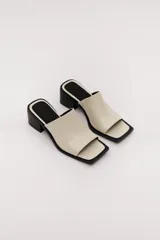 Sandalia marrón de cuero con punta cuadrada, talón abierto y faja ancha. Tiene detalle de elástico oculto en la cara interna de la capellada. El forro y la plantilla son de cuero vacuno.