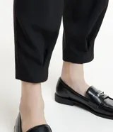 Pantalón negro de corte carrot, con pliegues delanteros, abotonado frontal y detalle en el bajo.