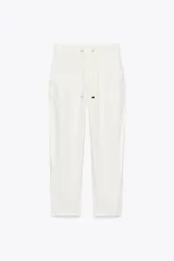 Pantalón jogger blanco de tiro medio con cintura elástica ajustable con cordones, bolsillos delanteros y falsos bolsillos de vivo en la espalda. El bajo es ajustable con botón a presión.