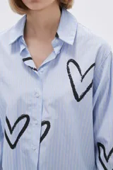 Camisa celeste a rayas verticales blancas, con cuello clásico, cierre frontal con botones y estampado de corazones negros.