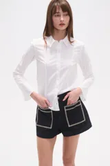 Camisa blanca de algodón, entallada, con cuello camisa y cierre frontal de botones. Presenta mangas largas con puños sencillos.