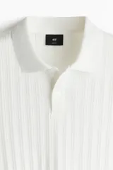 Remera polo blanca de punto texturizado de peso medio. Modelo de manga corta con cuello, tapeta de botones y bajo recto. Corte ajustado que realza el contorno del cuerpo creando una silueta entallada.