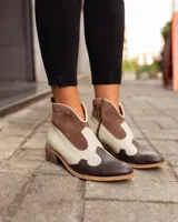 Botines de cuero marrón y blanco con diseño western, puntera redondeada y cierre lateral con cremallera. El talón tiene una tira de cuero para facilitar el calce.