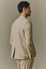Blazer color beige de corte slim fit, con solapas de muesca finas, botonadura sencilla con cierre de dos botones, bolsillo superior, bolsillos delanteros con solapa, tres bolsillos interiores, botones decorativos en los puños y abertura atrás.