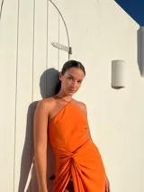 Vestido largo naranja de crepé con escote halter y falda tipo pareo con abertura lateral.