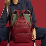Mochila bordeaux de símil cuero con cierres metálicos, doble bolsillo frontal, asa de mano y correas regulables en galón.