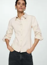 Camisa de jean color crudo, de corte entallado, con cuello camisero, mangas largas con puños abotonados y cierre frontal con botones.