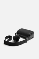 Bandolera negra con acabado grabado, compartimento principal con cierre mediante solapa imantada, bolsillo interior con cierre mediante cremallera, bolsillo frontal con cierre mediante cremallera, asa de hombro ajustable y monedero.