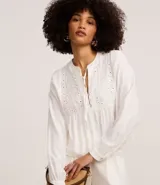 Blusa bata blanca de mangas largas, confeccionada en viscosa, con cuello padre con lazo y botones, bordado floral en el busto. 