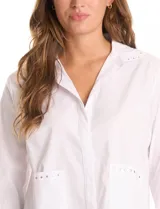 Camisa blanca de manga 3/4 con puños doblados, cuello en V y cierre de botones frontal. Presenta dos bolsillos delanteros con detalles de tachas metálicas.