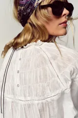 Camisa blanca de cuello redondo con detalle de nido de abeja y entredoses. Manga larga con bordados a tono y cierre trasero con botones.