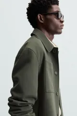 Sobrecamisa negra de corte amplio, con cuello solapa, manga larga con puños abotonados, bolsillos de parche en el pecho, bolsillos laterales y cierre frontal con botones.