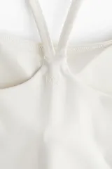 Top deportivo blanco con breteles finos cruzados en la espalda y logo de la marca en el centro del pecho.