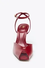 Sandalia de tacón fino color rojo, con tira delantera ancha, pulsera de tobillo con hebilla metálica y punta metálica.