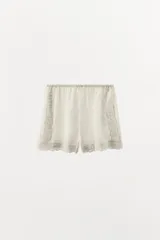 Shorts de tiro alto confeccionados en algodón color crudo, con cintura elástica, detalle de encaje, bordados y aplicación de abalorios a tono.