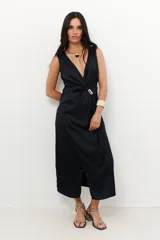 Vestido midi negro con escote en V, corte cruzado y detalle de hebilla dorada en la cintura.