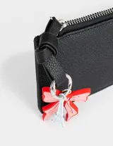 Monedero negro de cuerina con cierre circundante y charm colgante de moño rojo y torre Eiffel plateada.