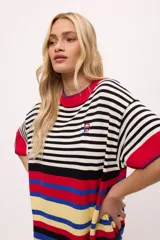 Vestido de tejido de punto color blanco y negro a rayas horizontales, con detalles en rojo y azul en el ruedo y cuello. Presenta cuello redondo con borde rojo y costuras decorativas azules.