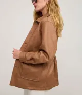 Campera estilo safari o sobrecamisa de mujer, color marrón camel, confeccionada en tejido que simula gamuza o cuero sintético. Presenta cuello camisa, cierre frontal de botones a presión, y cuatro bolsillos frontales con tapa (dos en el pecho y dos a la altura de la cadera). Tiene costuras visibles que definen el diseño.