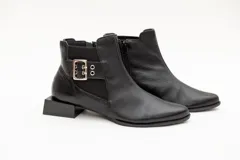 Botín de cuero negro con elásticos laterales, aplique metálico con ojales y cierre lateral con cremallera. Taco cuadrado desfasado de 3 cm.