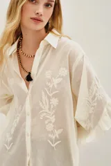 Camisa de algodón color blanco roto, con cuello camisero, mangas largas con volados y bordados florales en las mangas.