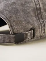 Gorra de gabardina color gris oscuro con visera curva y etiqueta con logo de la marca en el lateral.